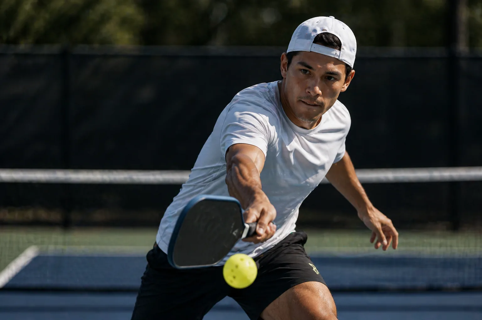 A pickleball player reaching forward through a focused shot on court